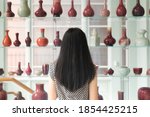 A chinese woman looking at a shelf of various vases within the walters art museum in baltimore maryland.