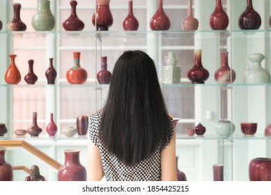 A Chinese Woman Looking At A Shelf Of Various Vases Within The Walters Art Museum In Baltimore Maryland.