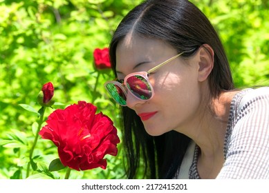 A chinese woman smelling a red peony in a garden on the island of Marthas vineyard in massachusetts on a sunny day. - Shutterstock ID 2172415201