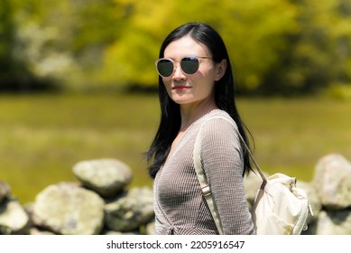 a chinese woman standing near a rock wall with blurred background at a park on martha's vineyard on a sunny day in new england. - Shutterstock ID 2205916547
