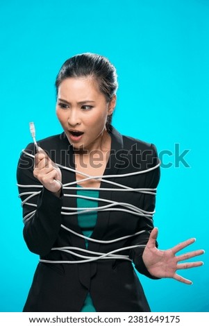 Chinese woman tangled up in computer network cable. Conceptual image. Young and fresh Asian female model a bright blue background.