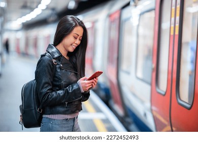 Chinese woman at underground train station using mobile phone - Young asian woman waiting for the train and smiling typing on the phone - Lifestyle and travel concepts - Powered by Shutterstock