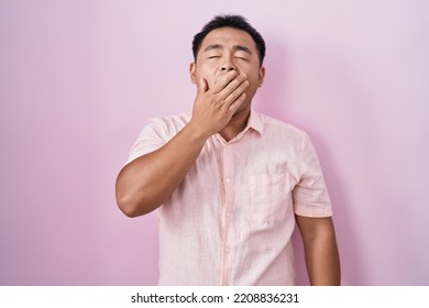 Chinese Young Man Standing Over Pink Background Bored Yawning Tired Covering Mouth With Hand. Restless And Sleepiness. 