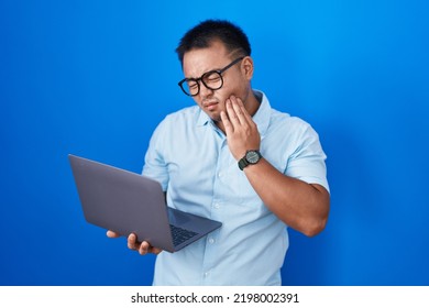 Chinese Young Man Using Computer Laptop Touching Mouth With Hand With Painful Expression Because Of Toothache Or Dental Illness On Teeth. Dentist Concept. 