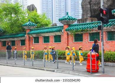 Chinese Young Students Of Elementary School Wearing Yellow School Uniform Are Going To Excursion With Teachers Along Ancient Brick Buddhist Temple Wall.Hong Kong,China,Feb 2013 