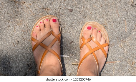 Chipped Nail Polish On  Toes In Sandals On Sandy Beach