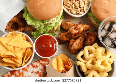 Chips, burgers and other fast food on white wooden table, flat lay