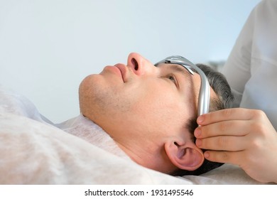 Chiropractor Doctor Is Putting On Electronic Headband From Migraine On Man's Forehead. Treatment Of Headaches With Electric Current In Clinic On Procedure With Manual Physiotherapist.