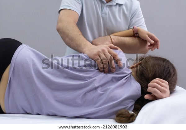 A chiropractor\
palpates the area of the scapula on the back of the patient.\
Appointment with an osteopath. The girl lies on the couch, the\
doctor works with her back. Back\
view
