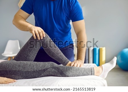 Chiropractor or physiotherapy specialist at rehabilitation center or massage room examining leg of young woman and checking her knee flexion. Cropped shot. Physical therapy, pain treatment concept