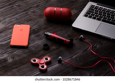 Chisinau, Moldova - February 20, 2018: Iphone In Red Case, Bluetooth Speaker, Mod Vape, Fidget Spinner, Headphones And Apple Macbook Pro On Wooden Desk