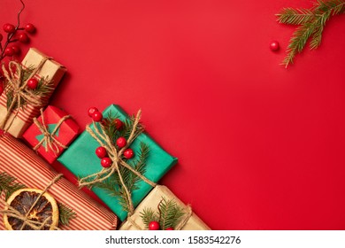 Chistmas background frame  with gift boxes,  decorated with spruce branches, holy berries and dried oranges on festive red,  top view, empty space for text