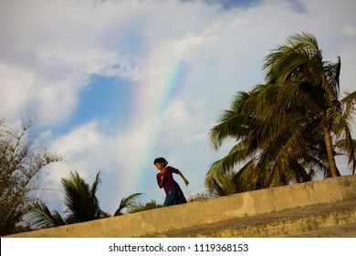 Chittagong, Bangladesh - 06 16 2009: Girl running in front of a rainbow as win blows