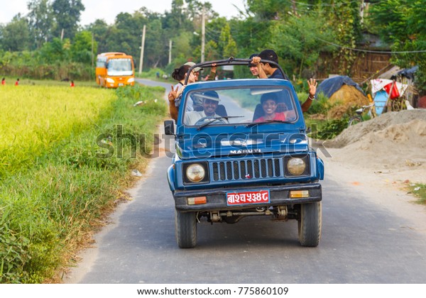 CHITWAN, NEPAL - September 27,\
2013: Smiling people in the car on the road in the Royal Chitwan\
National Park. The park is 932 sq. km, is mainly covered by\
jungle.