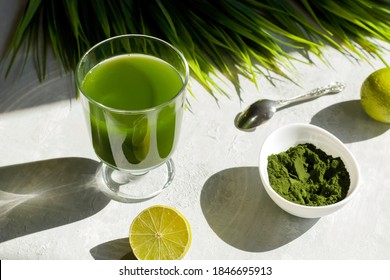 Chlorella detox healthy drink in glass with lime and powder on light background. Superfood, natural antioxidant for a green diet. Anti-aging effect. Hard shadows