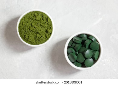Chlorella and spirulina closeup. Spirulina pills and chlorella powder in bowls on a white concrete background. Superfoods. Top view, flat lay.