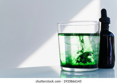Chlorophyll drops in water, sitting next to dropper bottle in sunlight