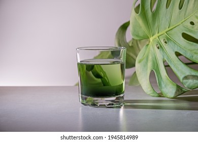 Chlorophyll Extract Is Poured In Pure Water In Glass Against A White Grey Background With Green Leaf. Liquid Chlorophyll In A Glass Of Water. Concept Of Superfood, Healthy Eating, Detox And Diet