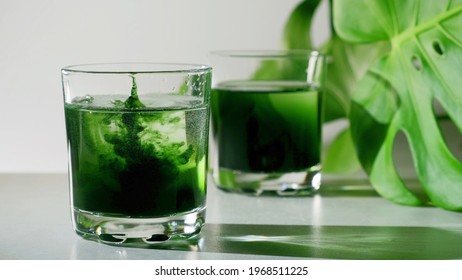 Chlorophyll extract is poured in pure water in glass against a white grey background with green leaf. Liquid chlorophyll in a glass of water. Concept of superfood, healthy eating, detox and diet