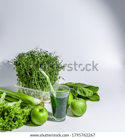 chlorophyll in a glass of water on a white background near are various fresh vegetables fruits and roots with lettuce and spinach