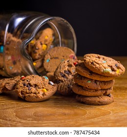 Choc Chip Smartie Cookies Falling Out Of Jar On Wooden Table Top.