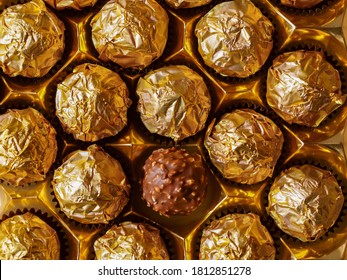 Chocolate balls in gold foil view from the top, one praline in open wrapper foil