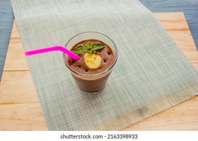 Chocolate Banana Shake Topping Sprinkled With Chocolate Chips, Banana And Mint Leaves With Straw On Cloth