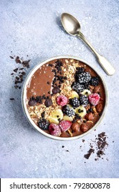 Chocolate banana smoothie bowl with frozen berries and granola on a light grey slate, stone or concrete background.Top view.