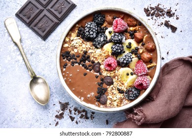 Chocolate banana smoothie bowl with frozen berries and granola on a light grey slate, stone or concrete background.Top view.