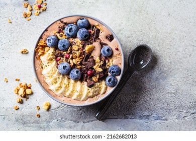 Chocolate banana smoothie bowl with granola, berries and hemp seeds, gray background, top view, copy space. Healthy raw vegan recipe concept. - Powered by Shutterstock