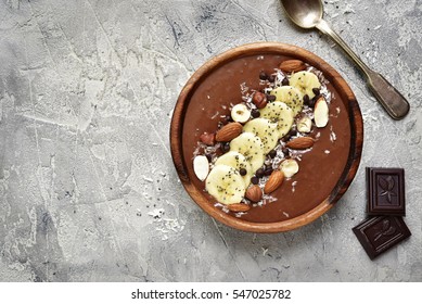 Chocolate banana smoothie bowl with nuts and chia seeds on a grey concrete,stone or slate background.Top view with copy space.