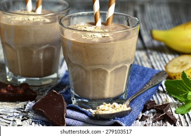 Chocolate and banana smoothie with oats in a glass on wooden table.