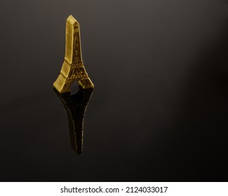 Chocolate Bonbon In The Shape Of A Golden Eiffel Tower. Plain Black Background