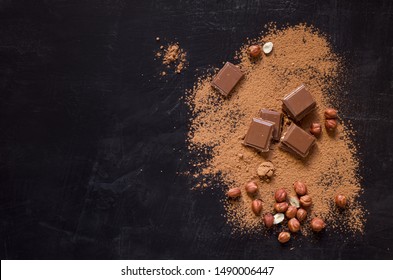 Chocolate broken pieces, cocoa powder and hazelnut on black rustic background with copy space, flat lay. - Shutterstock ID 1490006447