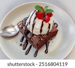 Chocolate brownie and a scoop vanilla ice cream with strawberry slices and mint leaves on top with a white table and white plate background