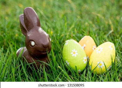 Chocolate Bunny In The Grass With Three Wrapped Easter Eggs