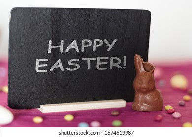 Chocolate Bunny Missing A Bite And Blackboard With The Text Happy Easter