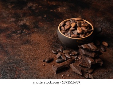 Chocolate and cacao concept. Cocoa powder in bowl near cocoa beans and broken chocolate on black background