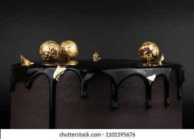 Chocolate cake with black glaze, decorated with balls in gold on a black background. Picture for a menu or a confectionery catalog.