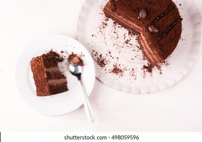 Chocolate Cake With Cream On A White Wooden Table. One Piece Of Cake Is On The Plate, Girl Eats It, Hand In The Picture, Top View, Copy Space