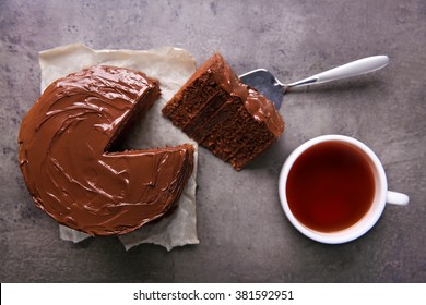 Chocolate Cake With A Cut Piece And Blade And Cup Of Tea On Gray Background, Closeup