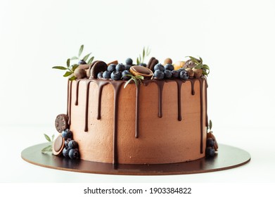 Chocolate cake decorated with blueberries, cookies and chocolates on a white background. Flat lay of the brown birthday cake