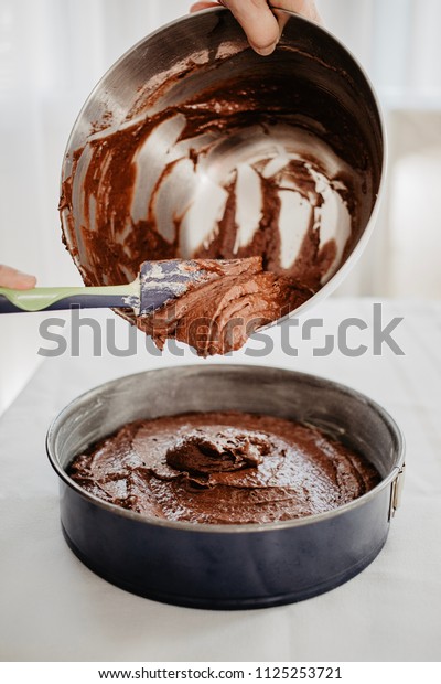 Chocolate cake dough being transferred into\
round-shaped baking tin with silicone spatula. Woman preparing\
chocolate cake to be baked. White\
background.