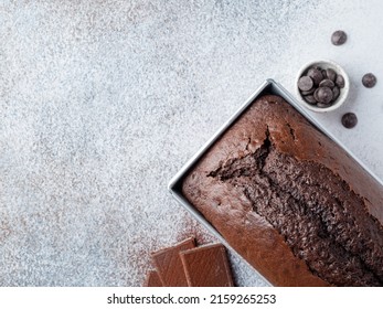 Chocolate cake in metal rectangular baking form with cocolate chips and pieces. Top view. Grey concrete background. Copy space. Homemade bakery concept. Moist sponge cake with cocoa powder.