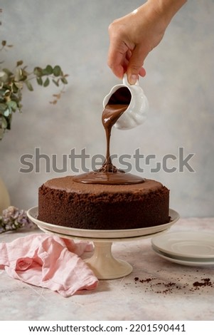 Chocolate cake. Pouring chocolate glaze on cake. Homemade chocolate cake on cake stand, home baking concept.