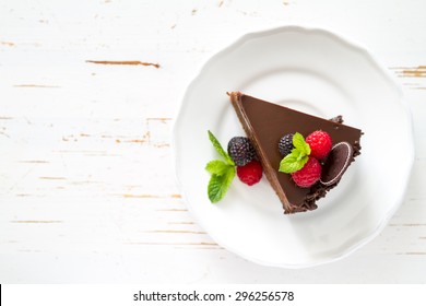 Chocolate cake with raspberry, blackberry, mint, white plate, white wood background, top view - Shutterstock ID 296256578