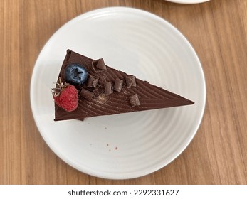 Pastel de chocolate con arándanos y bayas en un plato blanco con fondo de madera deliciosa y buena. Pastel de chocolate con vista superior.