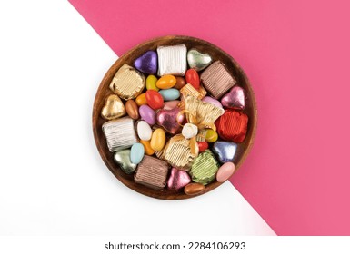 Chocolate candies, top view plate of chocolate candies. Wrapped multicolored foil. Almond candies. Isolated white and pink background. Copy space. Traditional Turkish feast called bayram sweets.