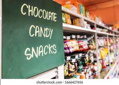Chocolate, Candy, Snacks signage at the aisle of supermarket with defocused merchandise on shelf