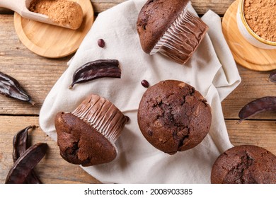 Chocolate carob cupcakes cooking with carob powder and dried carob pods and carob powder in a bowl over wooden background. Organic healthy sweet food for vegan vegetarian food and drinks, close up